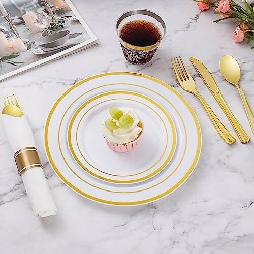 Elegant table setting with gold-rimmed plates, utensils, and a cupcake