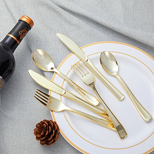 Gold flatware set on a plate with a wine bottle and pinecone.